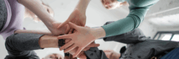 Menschen stehen im Kreis und legen ihre Hände übereinander. Es soll Resilienz in der Gemeinschaft signalisieren.